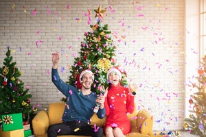 Man and woman on sofa in room of Christmas decorations with falling confetti
